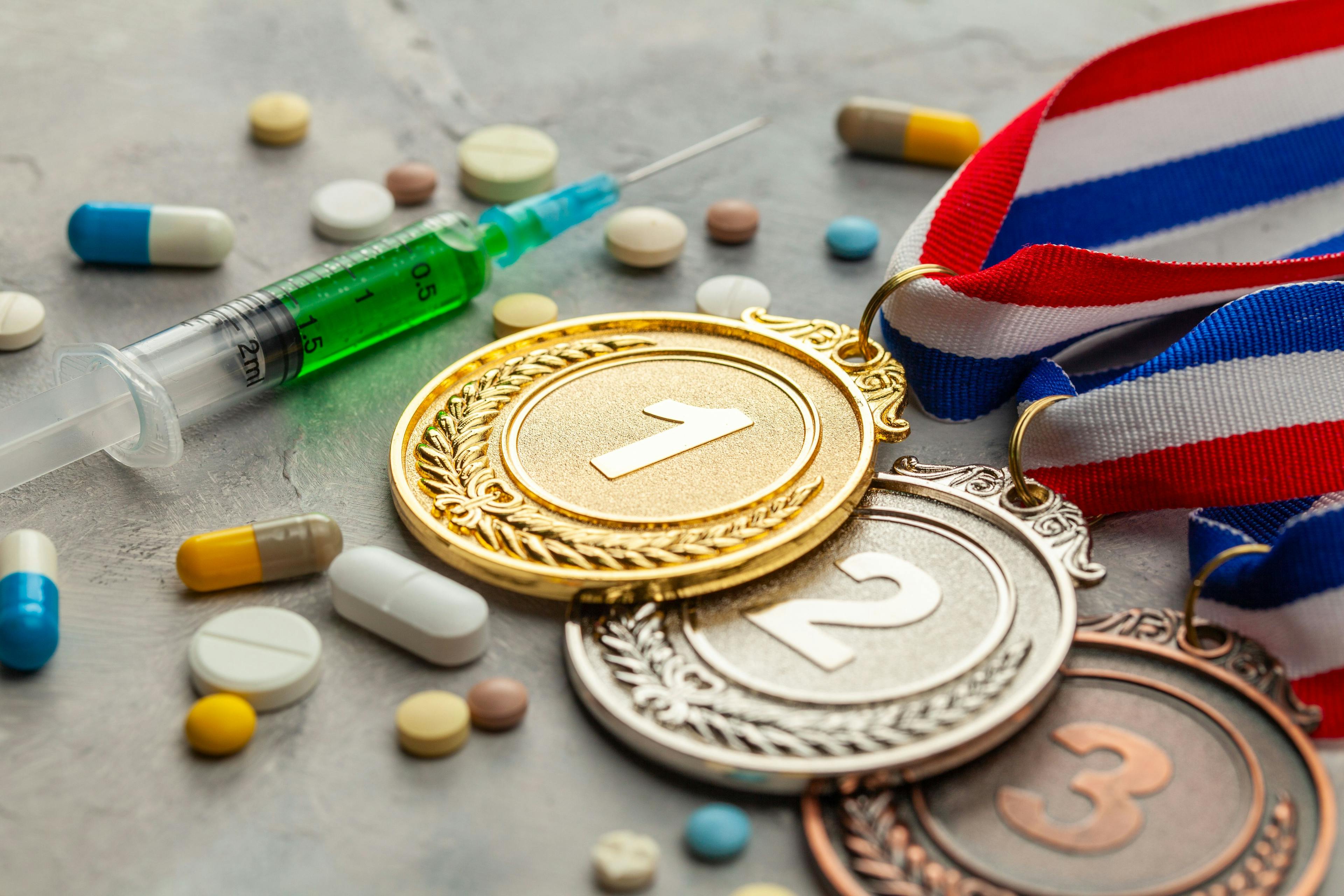 Doping for athletes. Golds, silver and bronze medal and doping syringe and pills with capsules on a gray background | Image Credit: © adragan - stock.adobe.com