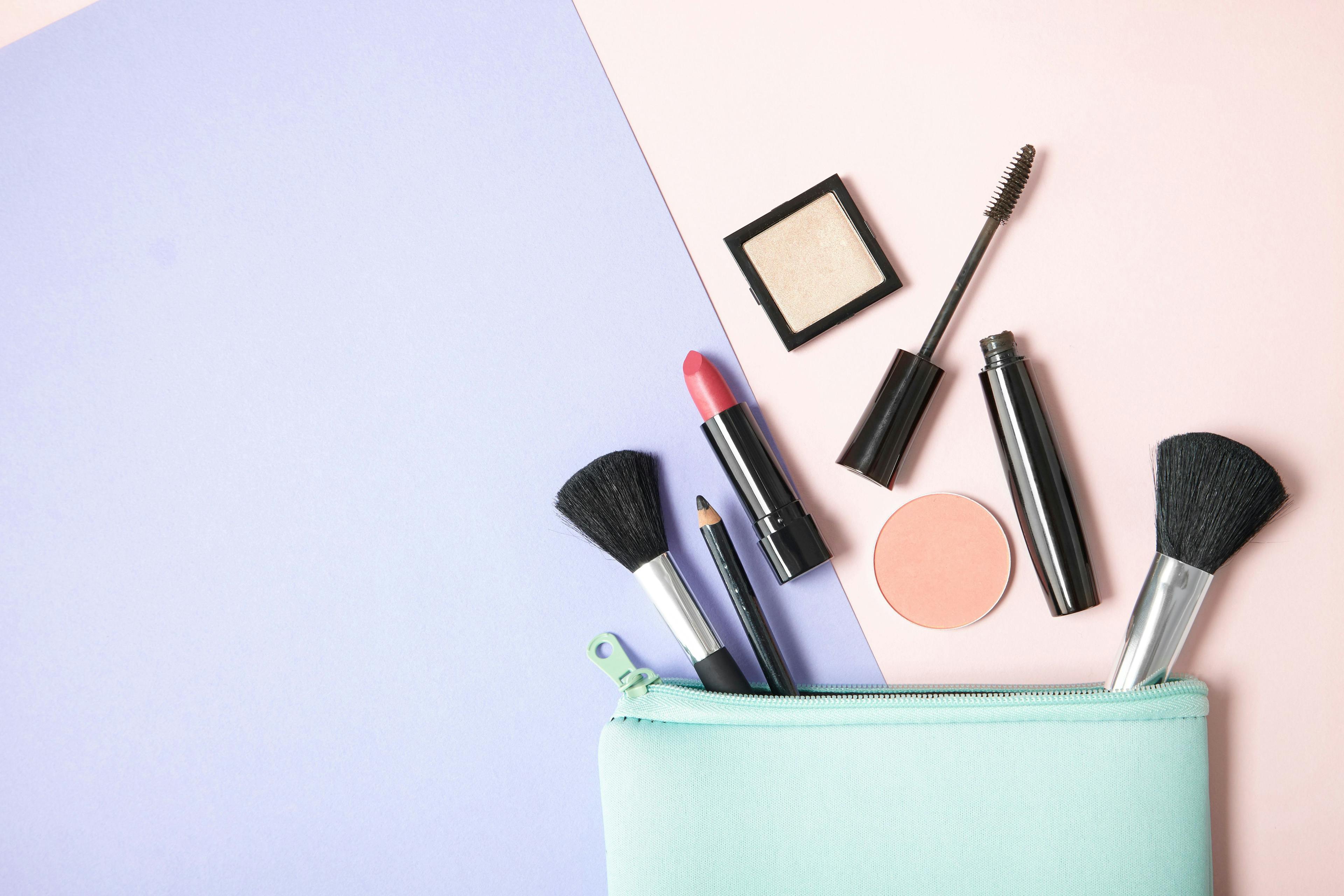 Make up products spilling out of a pastel blue cosmetics bag, on a pink and purple background with blank space at side | Image Credit: © beckystarsmore - stock.adobe.com 