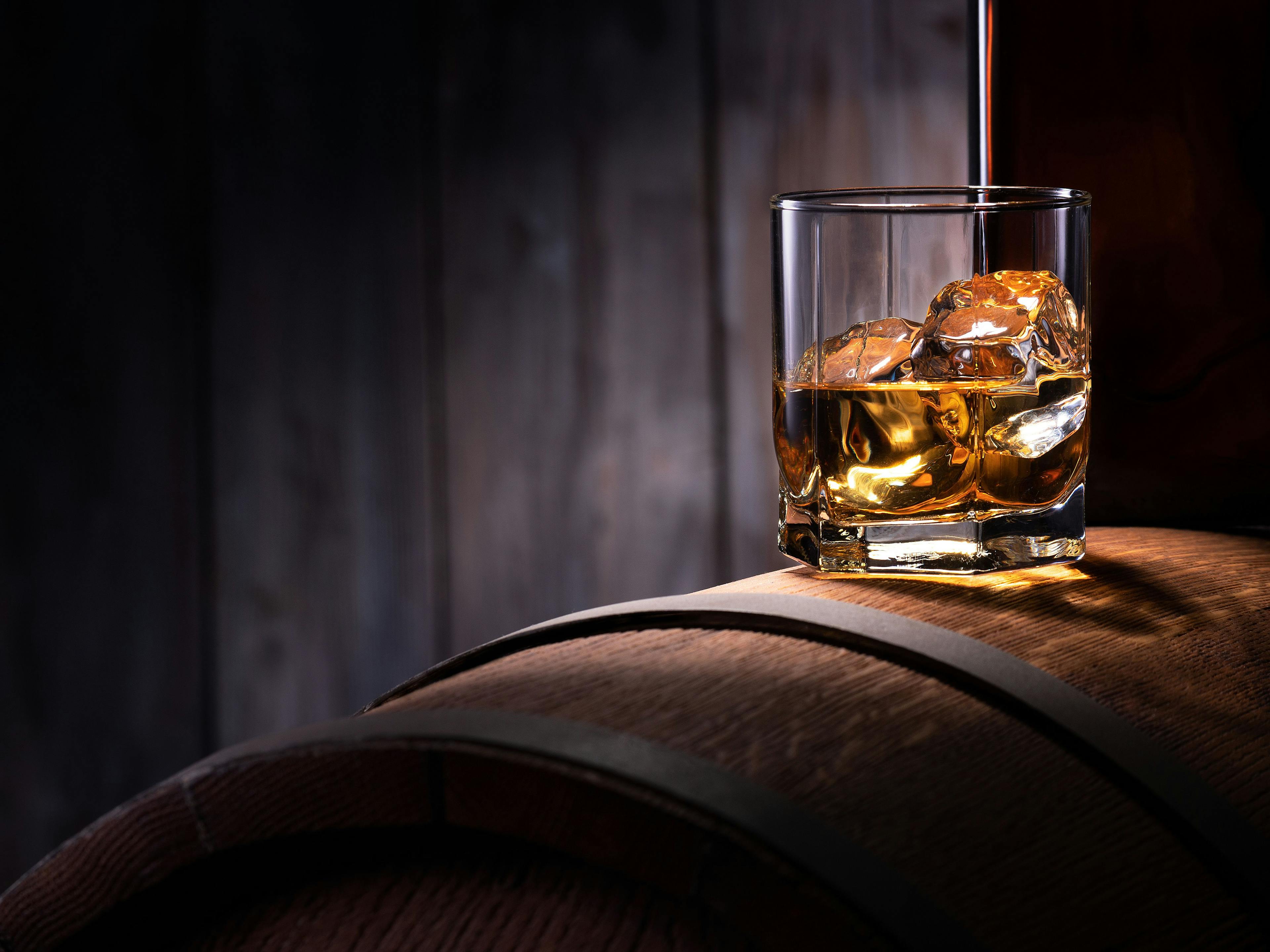 Glass of whiskey with ice cubes on the wooden barrel with wooden background | Image Credit: © Alexandr Steblovskiy - stock.adobe.com 