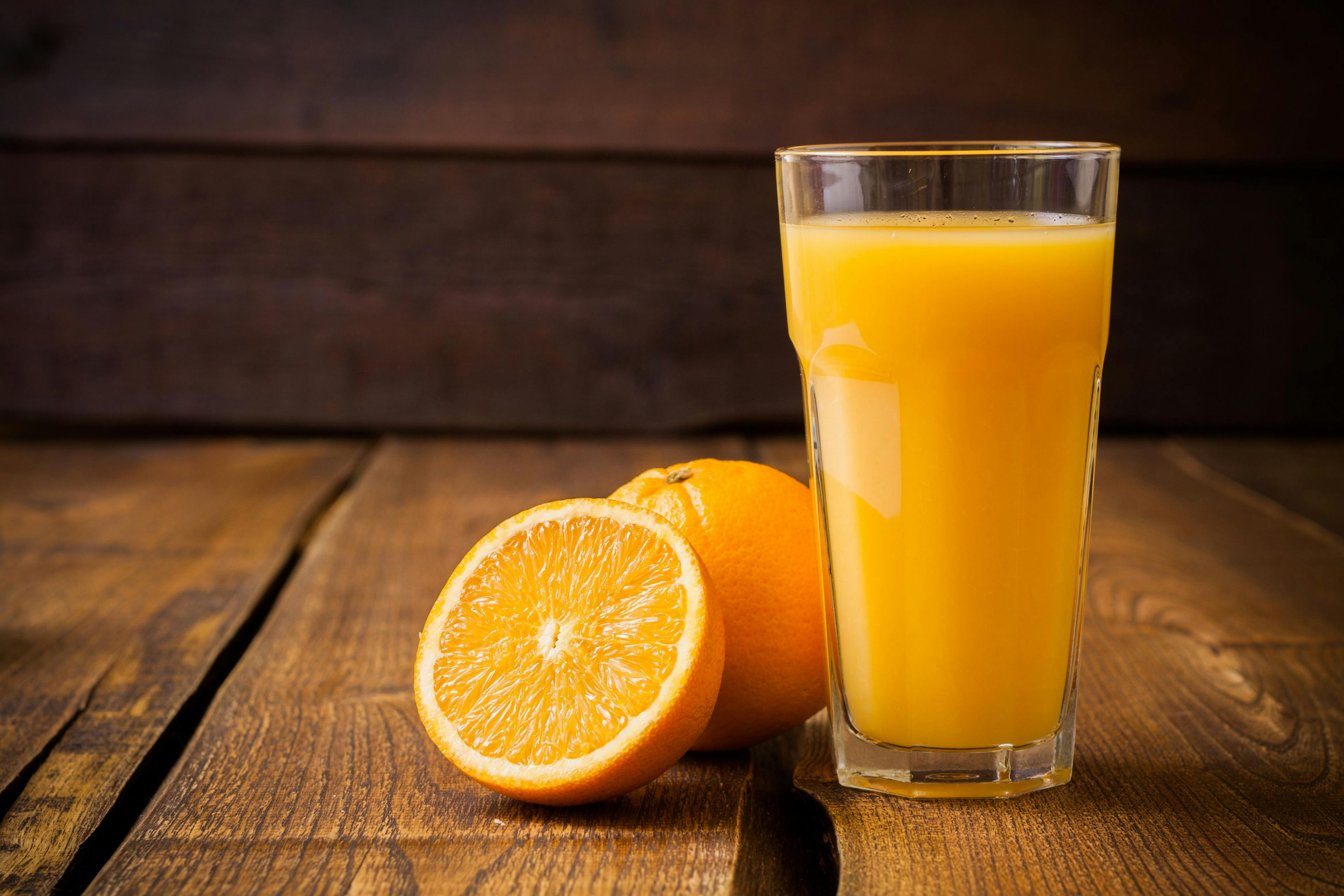 Orange fruit and glass of juice on brown wooden background | Image Credit: © avirid - stock.adobe.com.
