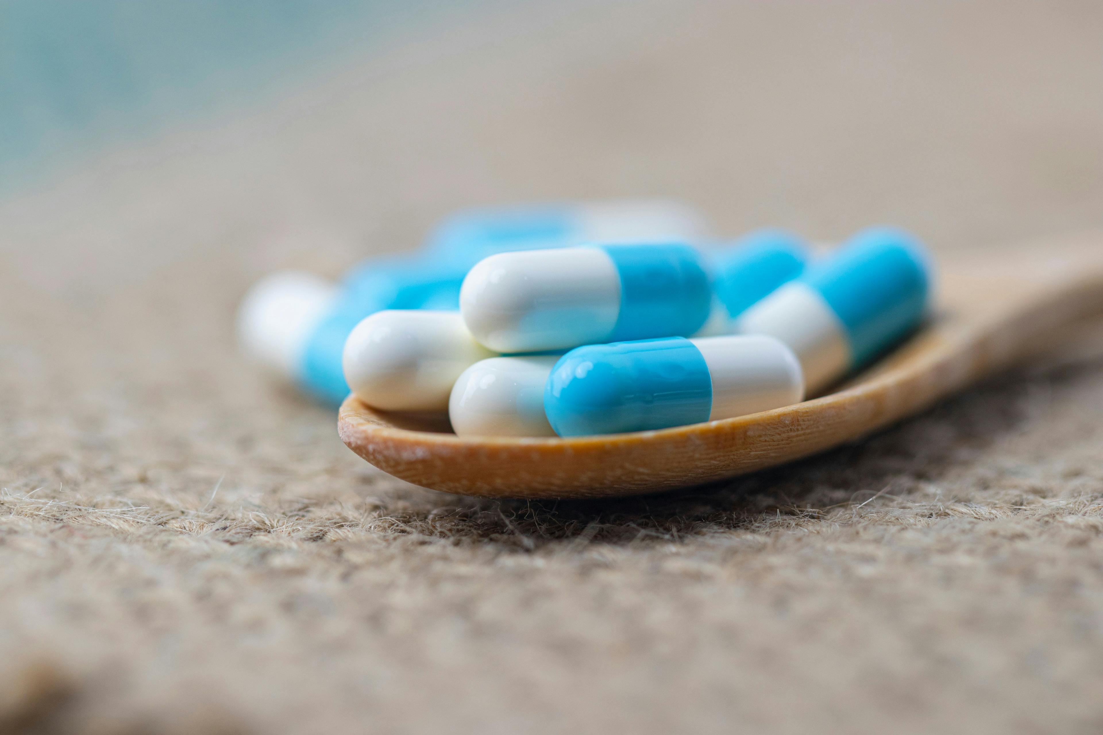 Close-up of blue medical capsules in wooden spoon on burlap sack background.