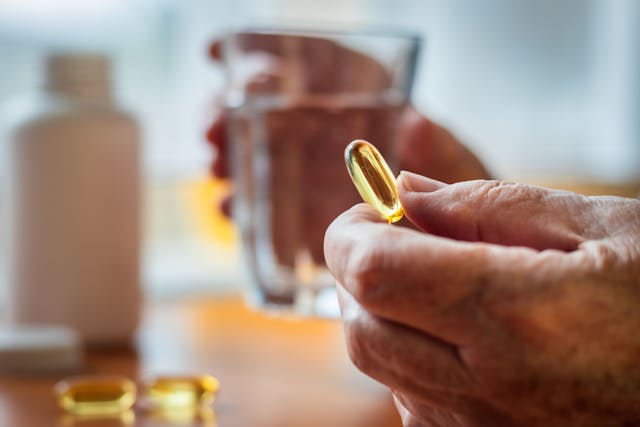 Senior woman holding omega-3 fish oil nutritional supplement and glass of water | Image Credit: © encierro - stock.adobe.com