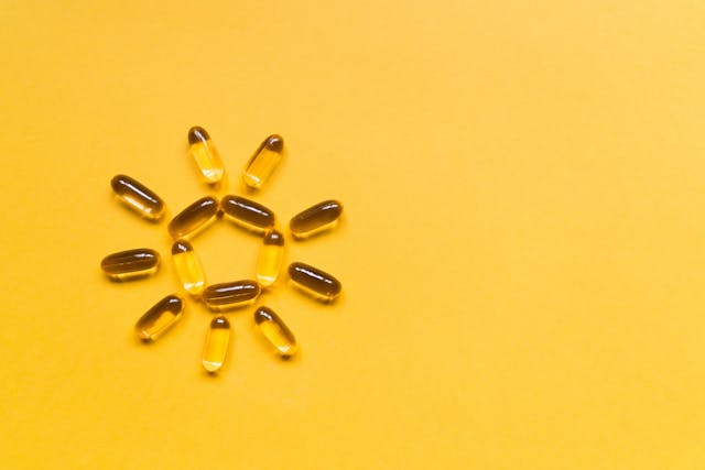 Close up capsules of fish fat oil in the sun shape, omega 3, vitamin e on the yellow background. Healthy food diet. Nutritional supplement | Image Credit: © MagicalKrew - stock.adobe.com