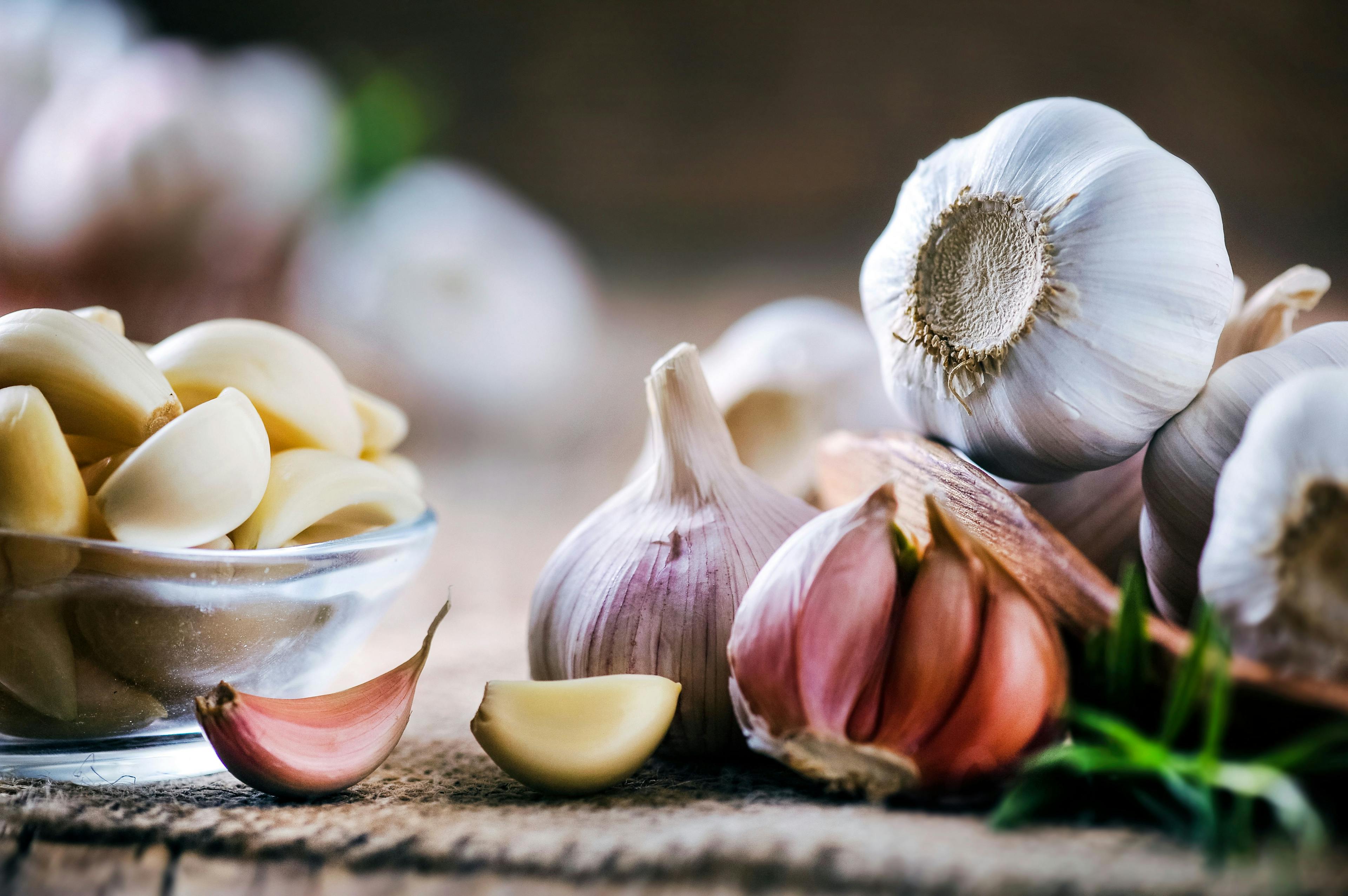 Garlic cloves on rustic table. Garlic in wooden bowl. Fresh peeled garlic and bulbs. | Image Credit: © Milan - stock.adobe.com