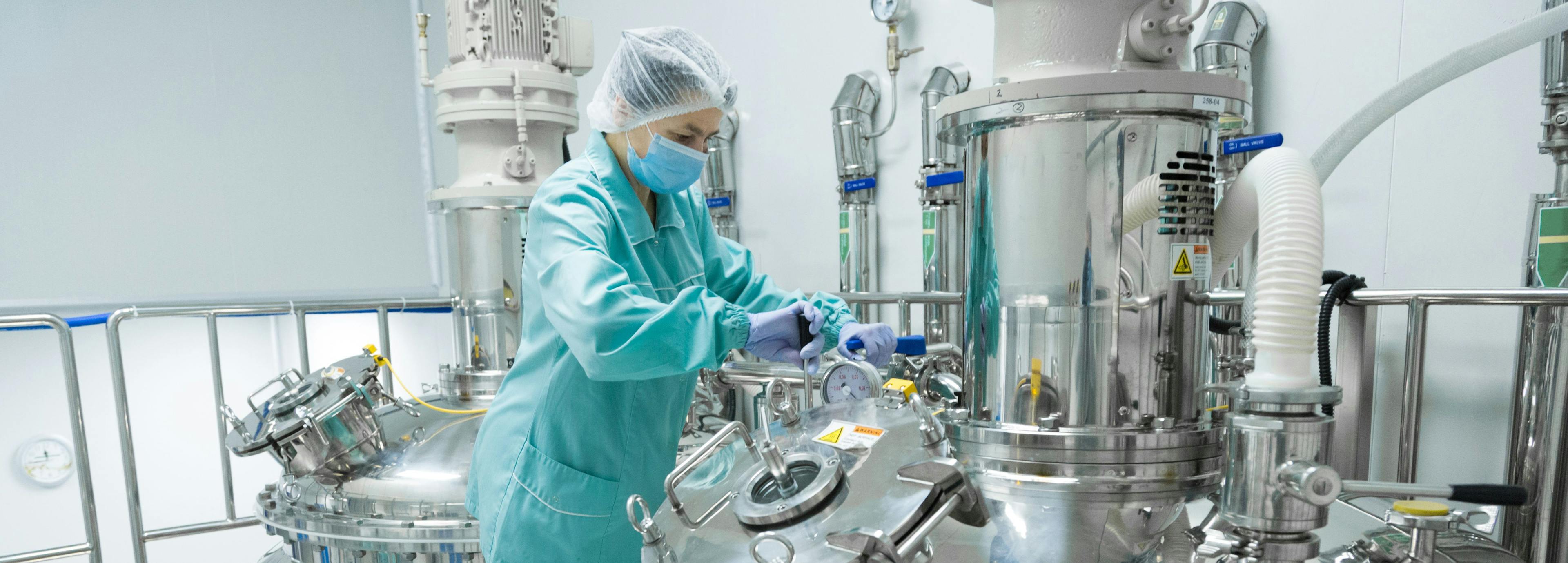 Pharmaceutical factory woman worker in protective clothing operating production line in sterile environment | Image Credit: © Ivan Traimak - stock.adobe.com