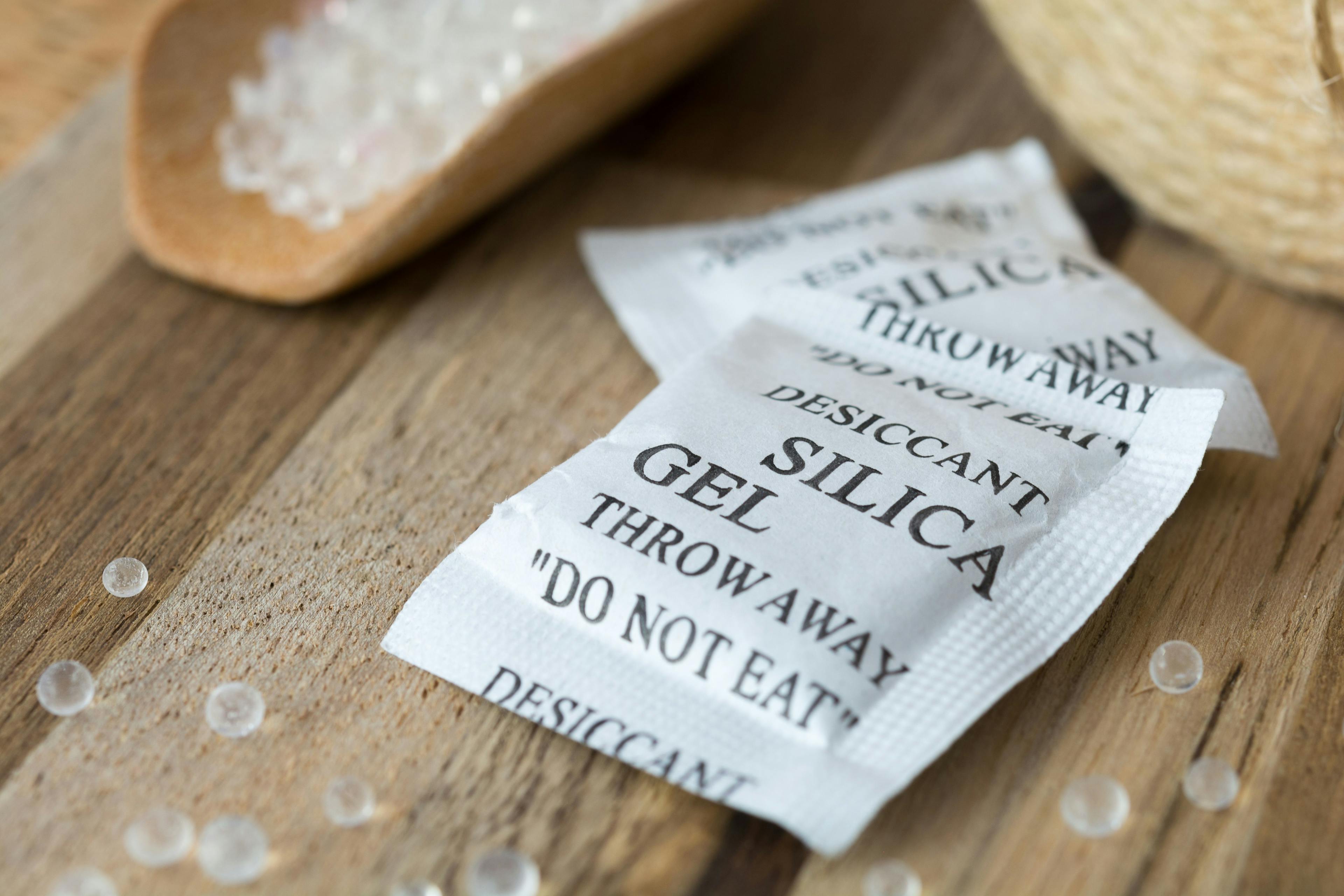 Desiccant or silica gel in white paper packaging and spread on the wooden background. | Image Credit: © mahnoionline - stock.adobe.com