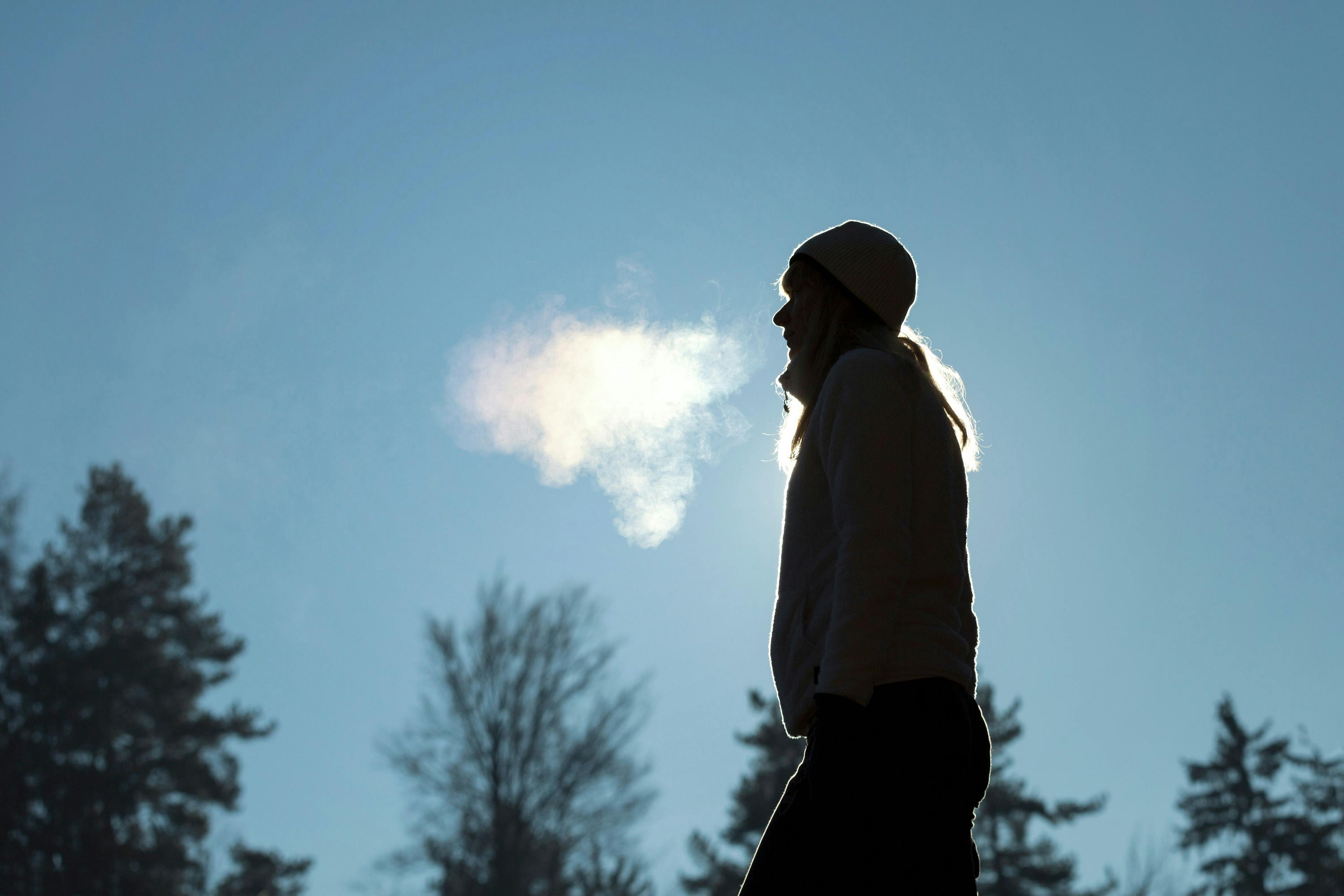 Silhouette of a woman with hat breathing warm air during a cold winter morning. Selective focus used. | Image Credit: © robsonphoto - stock.adobe.com