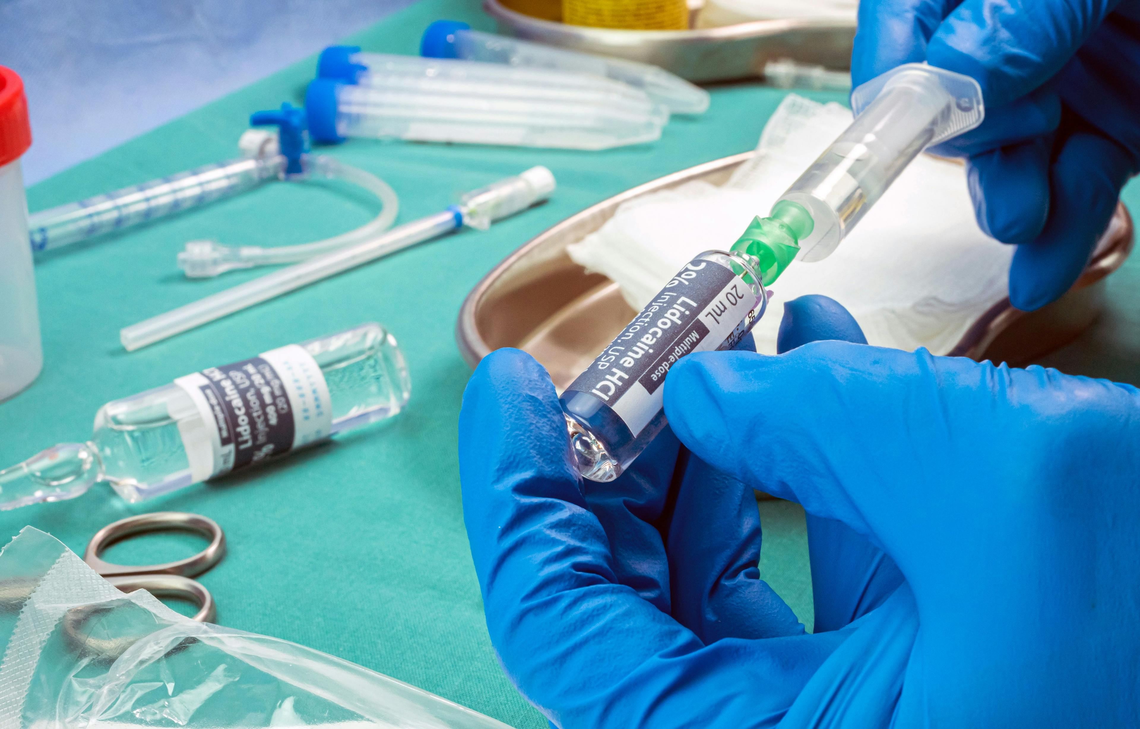 Nurse holds ampoule of anesthesia, preparation to extract cerebrospinal fluid to investigate causes in a person affected by transverse myelitis who was injected with experimental Oxford phase three | Image Credit: © Felipe Caparrós - stock.adobe.com