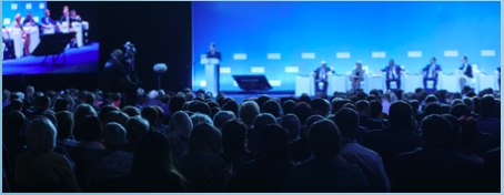 Speakers standing behind podiums on a stage in front of a large crowd.
