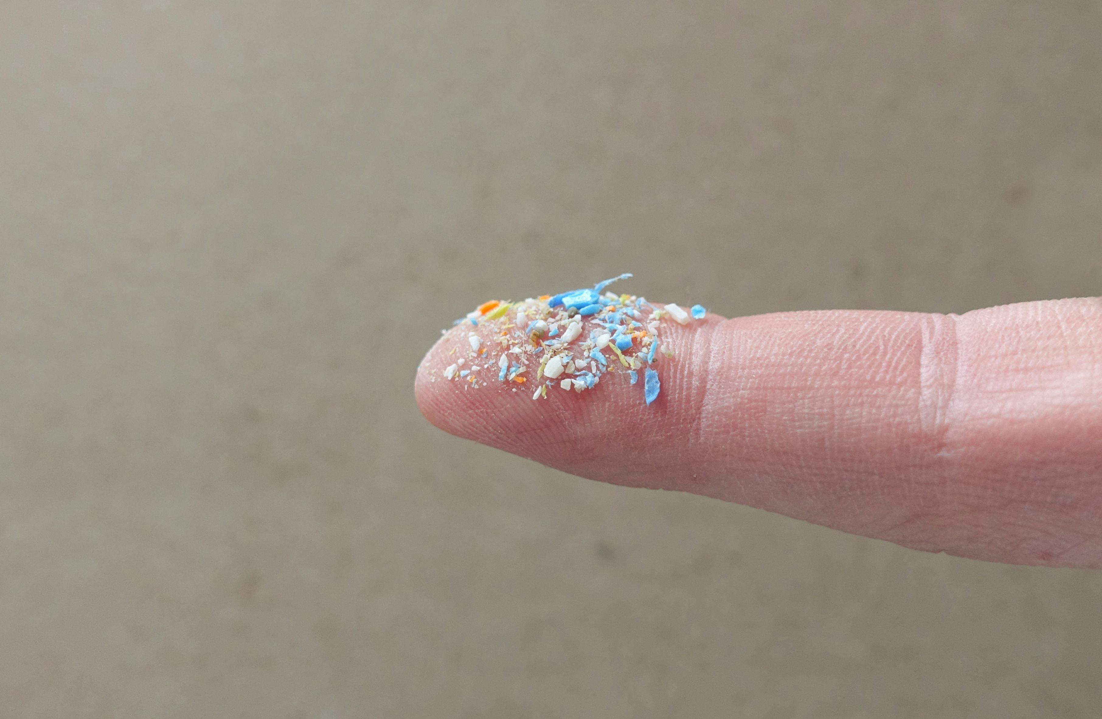 Close up side shot of microplastics on a human finger. Creative concept of water pollution and global warming. Climate change idea. A bunch of plastic rubbish that cannot be recycled. | Image Credit: © SIV Stock Studio - stock.adobe.com