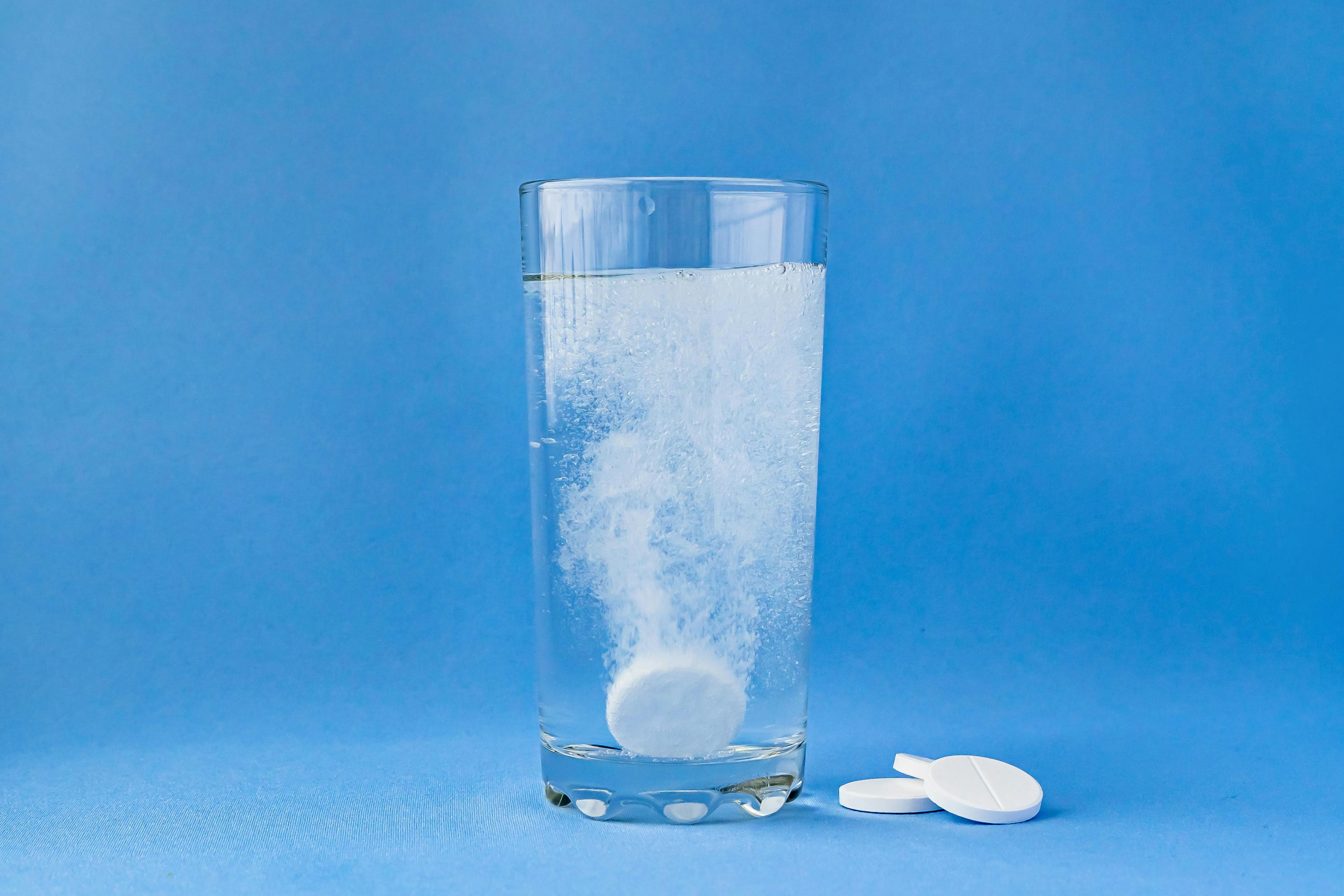 Fizzy aspirin in a glass of water on a blue background. Vertical format and soft focus. | Image Credit: © Natalia - stock.adobe.com
