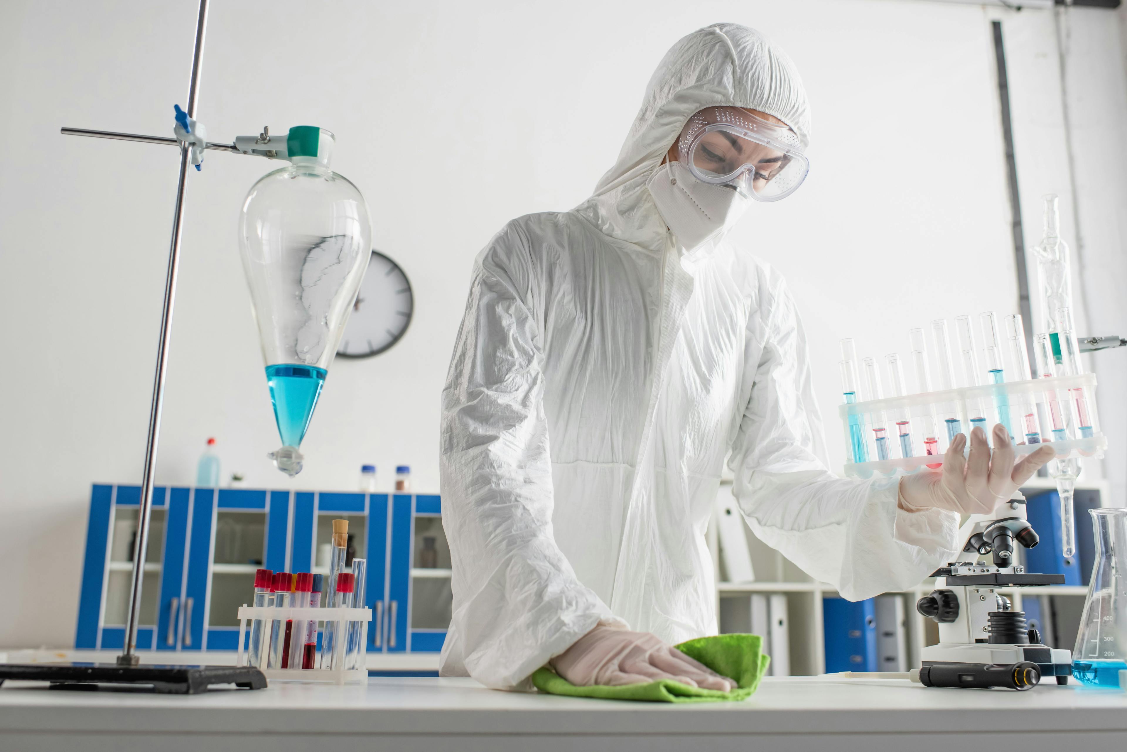 doctor in protective suit holding test tubes while wiping desk in laboratory. | Image Credit: © LIGHTFIELD STUDIOS - stock.adobe.com