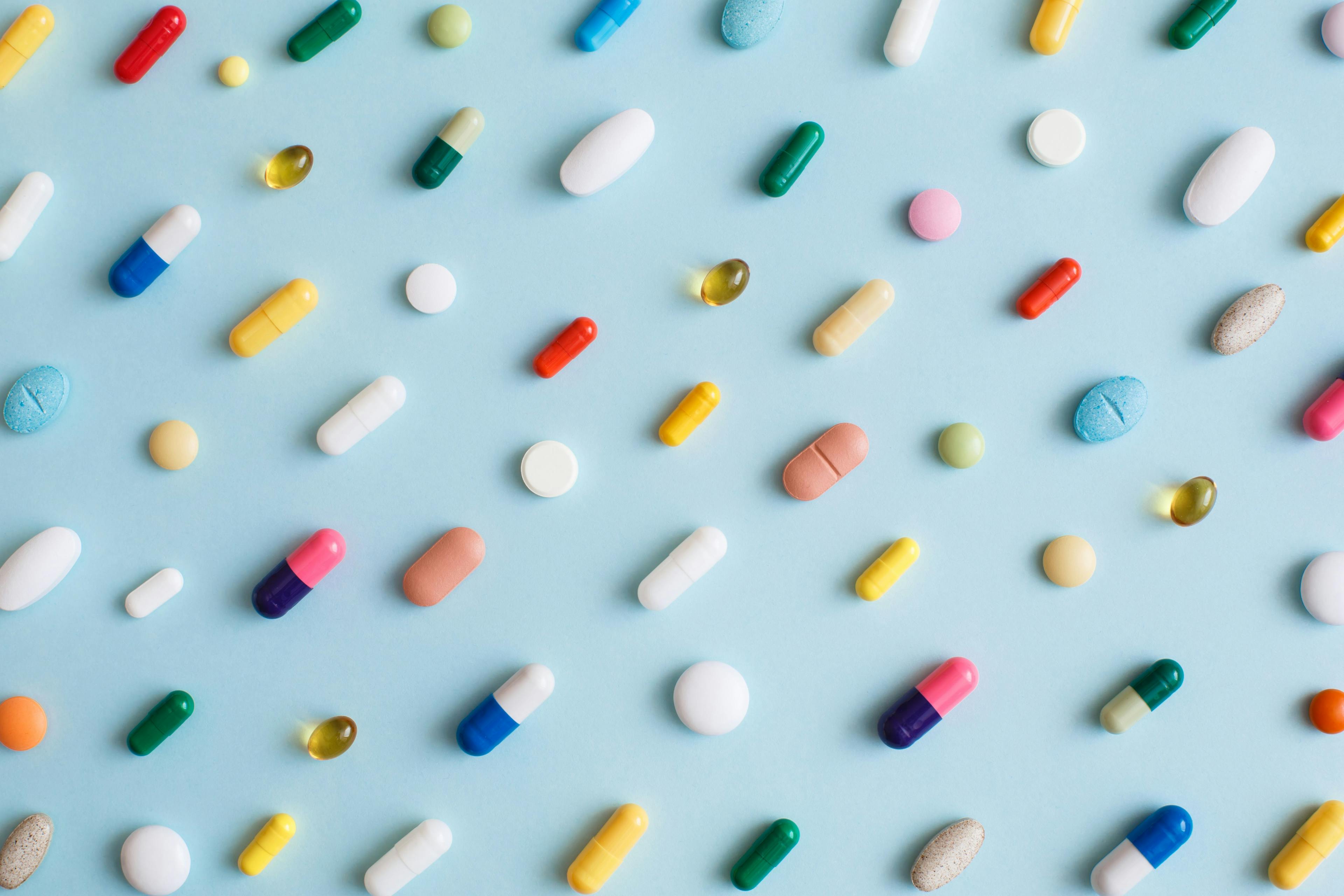 Creative layout of colorful pills and capsules on blue background. Minimal medical concept. Pharmaceutical, Covid-19 or Coronavirus. Flat lay, top | Image Credit: © Tatiana - stock.adobe.com