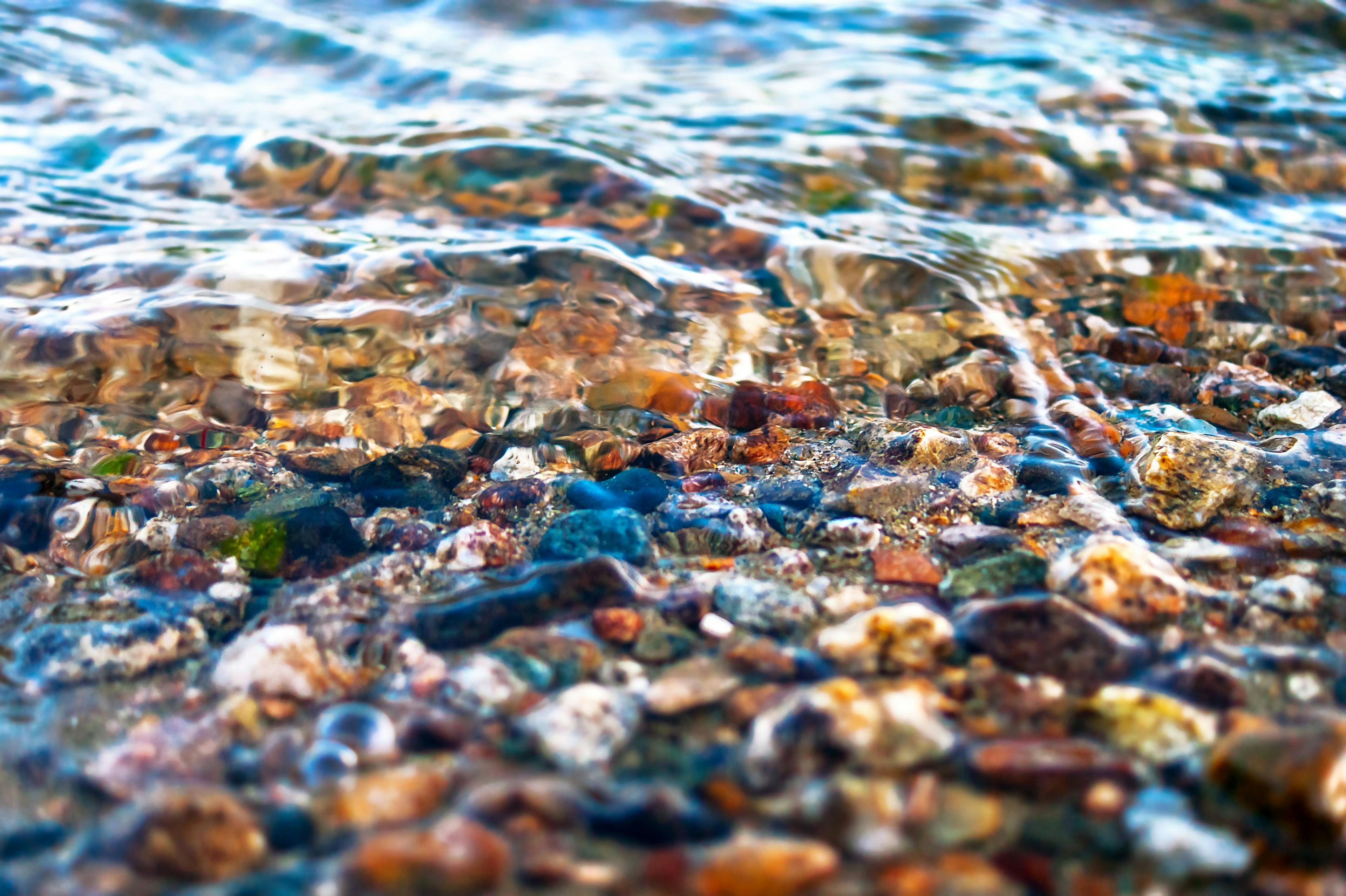 Close-up View of Colorful Pebbles in Water Waves. Travel Concept | Image Credit: © Eugene Put - stock.adobe.com